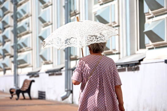 Ältere Dame geht mit Sonnenschirm auf der Straße